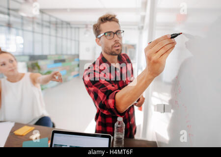 Casual young executive giving a presentation on white board to coworkers. Businesspeople discussing business ideas on white boar Stock Photo