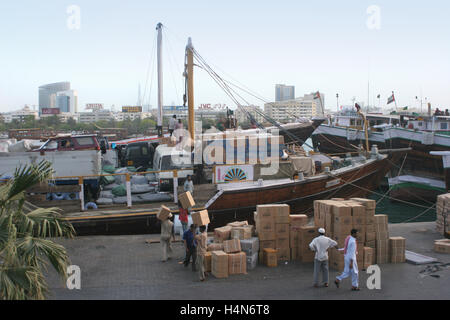 Boxes are manually loaded onto a  traditional timber cargo ship moored in The Creek in Dubai. City skyline in the background Stock Photo