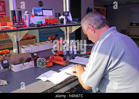 A middle-aged engineer makes notes as he repairs and services power tools at a workbench Stock Photo