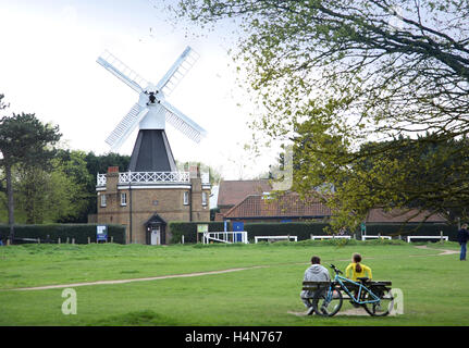 The windmill on Wimbledon Common in South London, UK, now a local museum of local history. SA couple sit on a bench with bicycle leaning behind. Stock Photo