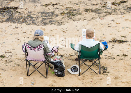 Couple reading on beach. Stock Photo