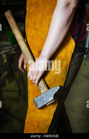 A blacksmith in a heatproof apron holding a large hammer. Stock Photo