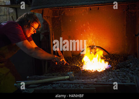 A blacksmith using tongs to heat something in a furnace. Stock Photo