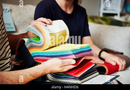 Two people sitting on a sofa, looking at a selection of fabric samples. Stock Photo