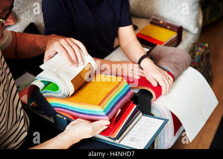 Two people sitting on a sofa, looking at a selection of fabric samples. Stock Photo
