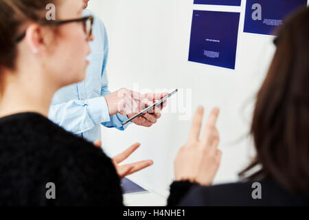 Three people using a smart phone beside a wall covered in posters. Stock Photo
