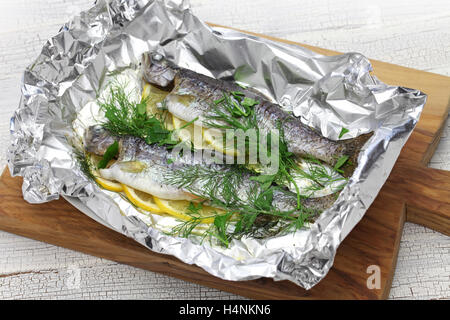 whole rainbow trout baked in foil on cutting board Stock Photo