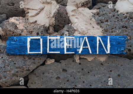 El Cotillo, Fuerteventura, Canary Islands, North Africa, Spain: hand made decorations, a wooden panel with the written Ocean hanging on black rocks Stock Photo