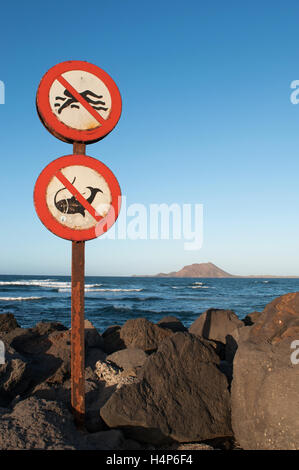 Fuerteventura: a sign prohibiting swimming and fishing in the port of Corralejo with view of the little island of Lobos on the background Stock Photo