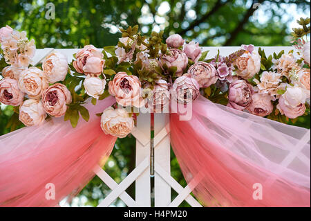 Beautiful white wedding arch decorated with pink and red flowers outdoors Stock Photo