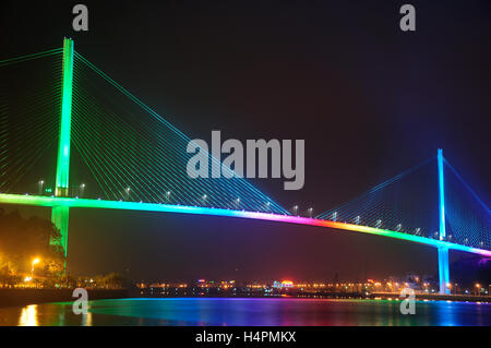 The Bai Chay Bridge in HaLong Vietnam lit up with rainbow colored lighting at night reflecting in Ha Long Bay. Stock Photo