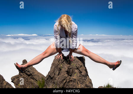 Young blonde woman acrobat making splits on rock on mountain's summit. Stock Photo