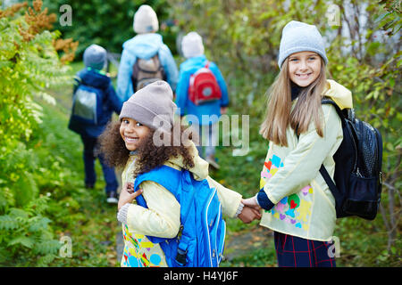 Two happy girls with backpacks looking at camera while walking to school Stock Photo