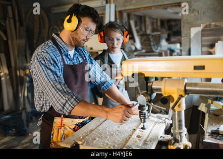 Carpenter in uniform and protective headphones working by drill machine Stock Photo