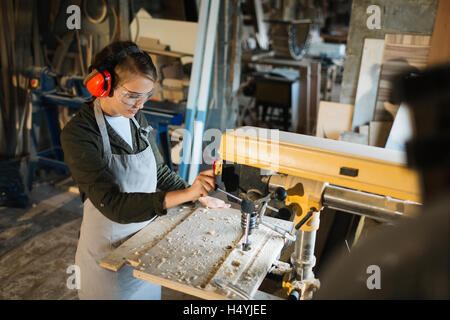 Female in uniform of carpenter using drill-machine in workshop Stock Photo