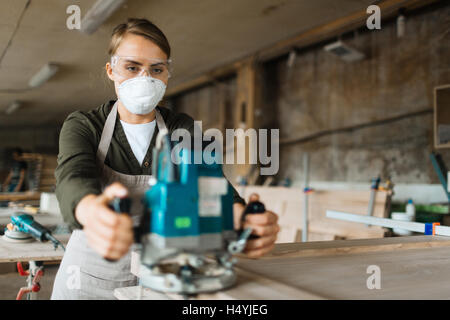 Female carpenter in protective eyeglasses and respirator working with sander Stock Photo