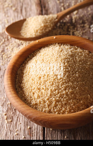 Raw couscous in a wooden bowl with a spoon and scattered on the table. vertical Stock Photo