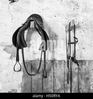 Old saddle and bridle hanging in a stable Stock Photo