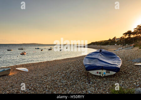 Sunset at Ringstead Bay, Dorset, UK, sailing boats moored in the bay and a tarpaulin-covered dinghy on the shingle beach in the foreground Stock Photo