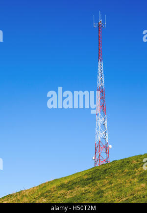 Tall communication tower on a green hill with blue sky background and copy space. Stock Photo