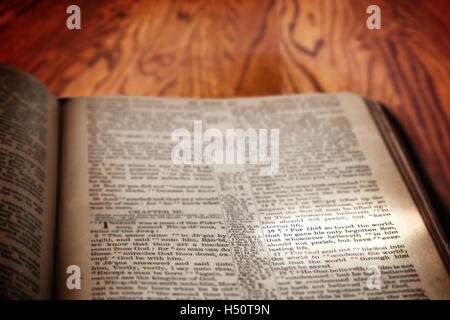 Closeup of an old Holy Bible opened to the famous verse of John 3:16 and highlighted by a beam of light. Book on a rustic table. Stock Photo