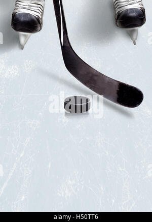 Hockey stick and puck on ice with a player's skates showing partically and copy space. Vertical orientation. Stock Photo