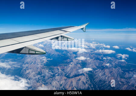 Airplane window view showing wing of plane flying over clouds and Rocky Mountains. Stock Photo