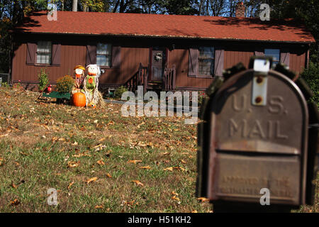 Outdoor fall decoration with scarecrow and pumpkins. Simple wooden house in countryside with mailbox in foreground. Stock Photo