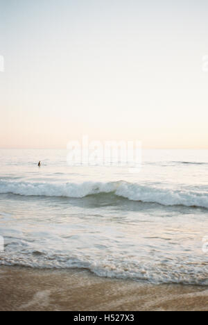 Ocean wave rolling onto a sandy beach, person in the background. Stock Photo