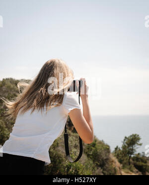 Teenage girl with long blond hair looking through a camera, taking a picture. Stock Photo