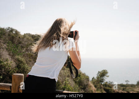 Teenage girl with long blond hair looking through a camera, taking a picture. Stock Photo