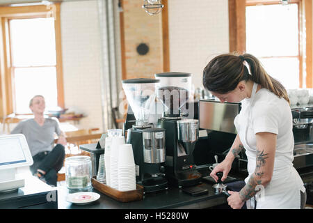 Woman wearing a white apron, in front of espresso machine, holding a portafilter. Stock Photo