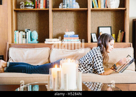 Woman with long brown hair lying on a sofa, reading a book. Stock Photo