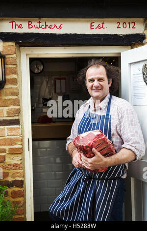 Butcher in blue striped apron holding a large piece of beef. Stock Photo