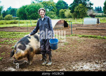 A woman stood by a large pig holding a bucket. Stock Photo