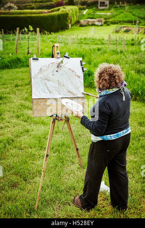 A woman artist outdoors at easel, applying paint on paper with a brush. Stock Photo