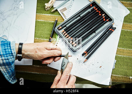 A person using a sharp blade, a craft knife, to sharpen lead pencils. Sketches on paper. Stock Photo