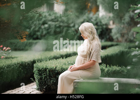 Portrait of a pregnant woman with long blond hair in a garden. Stock Photo