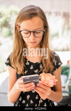 Girl with spectacles holding cell phone and rose. Stock Photo