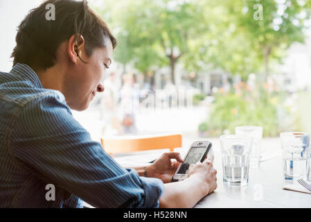 Woman with short brown hair sitting in a cafe, using a mobile phone. Stock Photo