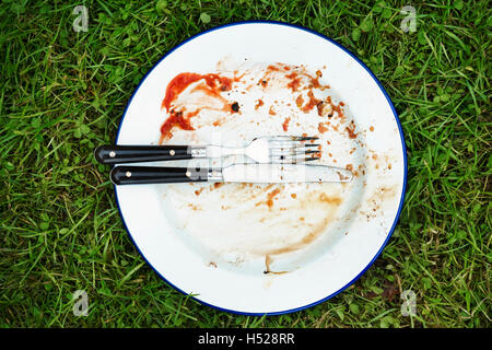 High angle view of dirty plate with knife and fork on a lawn. Stock Photo
