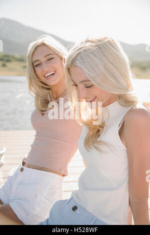 Portrait of two blond sisters sitting on a jetty. Stock Photo