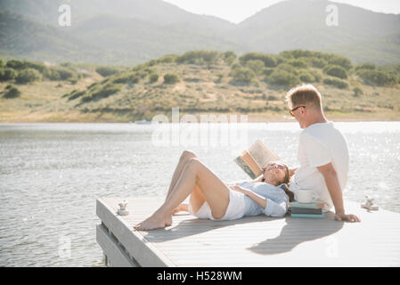 Man and woman reclining on a jetty, reading a book. Stock Photo