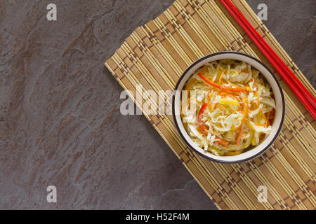 Korean salad of cabbage, carrots, sweet peppers - kimchi in an Asian style on the stone background, selective focus. Stock Photo