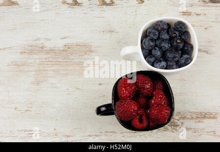 Two cups of black and white with fruit blueberries and raspberries on old wooden table. Close, flat view from above. horizontal Stock Photo