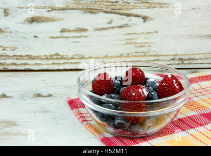 Raspberries and blueberries with the sugar in a glass bowl on an old, bright, wooden countertop, side view. Close, horizontal vi Stock Photo