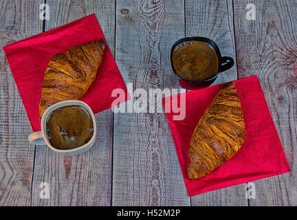 Two croissants and two cups of black coffee on red paper napkins stand on an old wooden table in vintage style. Photo filter eff Stock Photo