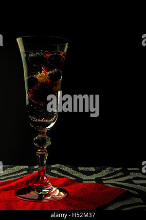 Sparkling water with raspberries, blueberries and grapes in a high glass on red serwetve and black background. Clearly visible g Stock Photo