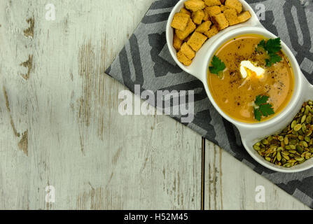 White dish with pumpkin soup, pumpkin seeds and small, baked croutons of bread, prepared the fresh leaves of parsley and cream a Stock Photo