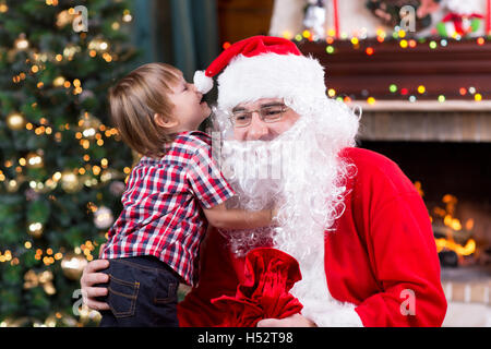 Santa Claus and child with presents at fireplace. Kid boy and father in Santa costume and beard Stock Photo